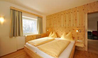 A cozy bedroom with two beds and wooden decor. Daylight streams in through the window, and the curtains are in soft colors.