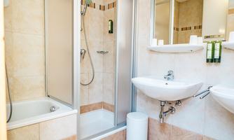 A modern bathroom with a shower and a bathtub. The walls are tiled in light colors, and there is a sink with a large mirror.
