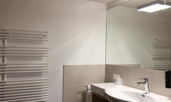 A modern bathroom with a round sink and a large mirror. There is a towel radiator on the wall.