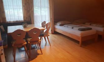 A cozy room with two single beds and a table with chairs. Large windows provide plenty of natural light.