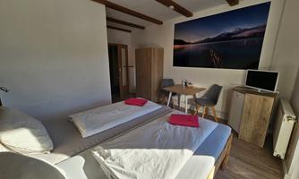 A bright room with two beds, a small dining area, and a television. A large landscape picture hangs on the wall.