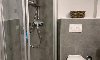 A modern bathroom with a shower cabin and a toilet. The walls are in gray colors, with a window that lets in daylight.