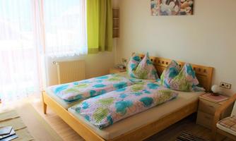 A cozy bedroom with a double bed and colorful bedspreads. Large windows let in plenty of daylight, and the walls are painted in warm colors.
