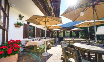 An inviting outdoor area of a restaurant with sun umbrellas and wooden chairs. Colorful flowers and sunlight create a cozy atmosphere.