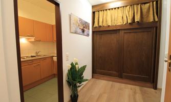 An inviting hallway with wooden walls and a modern kitchen entrance. A plant stands on the floor, adding a fresh touch.