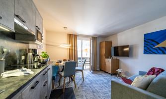 A modern apartment with an open kitchen and a cozy dining area. The living room is bright and inviting with a TV and a large window.