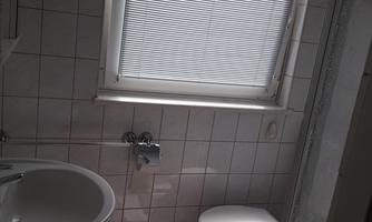 A modern bathroom with a sink and a toilet. Bright tiles and a window with blinds create a pleasant atmosphere.