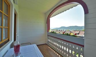 A cozy balcony with a table and two glasses. In the background, gentle hills and a clear sky can be seen.