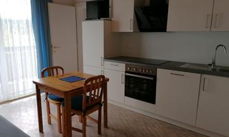 A cozy kitchen with a wooden table and chairs. The furniture is modern and bright, with plenty of daylight streaming in through the windows.