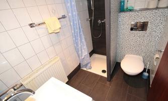 A modern bathroom with a shower, a sink, and a toilet. The walls are tiled, and there is a towel rack as well as a shower curtain.