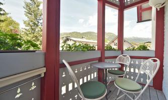 A beautiful balcony with two chairs and a small table. In the background, mountains and a green landscape can be seen.
