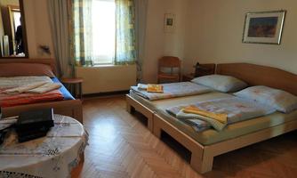 A simple room with two single beds and an additional bed. The room has a window with curtains and a small table.