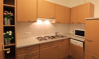 A modern kitchen with bright wooden furniture. It includes a stove, a microwave, and some potted plants.