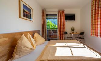 A cozy bedroom with a large bed and two pillows. Through the window, you can see a beautiful view of the greenery.