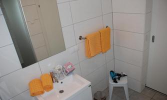 A modern bathroom with white tiles and a sink. Towels in bright orange are hanging on the wall.