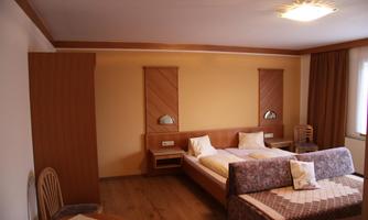 A simple room with two beds and wooden furniture. There is a table and chairs as well as a large window that lets in daylight.