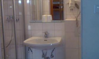 A small bathroom with a shower cabin, a sink, and a toilet area. The walls are tiled, and there is a mirror above the sink.