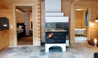 A cozy room with a wood stove and a stone tile. In the background, doors to other rooms and a bathtub are visible.