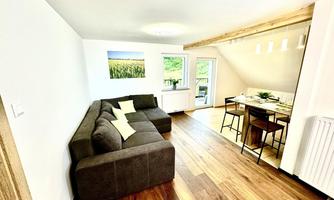A modern living room with a comfortable sofa and a dining area. 

Large windows bring in plenty of light and offer a view of the greenery.