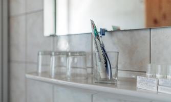 A bathroom shelf with a glass containing a toothbrush. Next to it are several empty glasses and small packages.