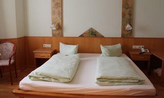 A simple room with a large bed and two pillows. In the background, there are cozy wooden details and a small table with a chair.