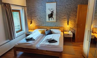 A cozy bedroom with a double bed and wooden floor. The walls are lined with stones, and a picture of a moose hangs above the bed.
