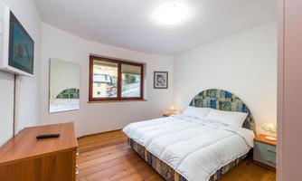 A beautiful bedroom with a large bed and wooden floor. There is a window, a television, and a nightstand.
