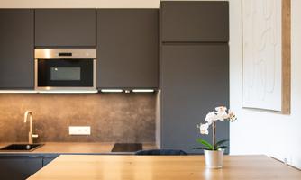 A modern kitchen with gray cabinets and a wooden countertop. On the table sits a small orchid.