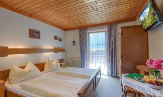 A cozy bedroom with a wooden ceiling and two beds. The room has large windows that let in plenty of daylight and is adorned with flowers and fruit.