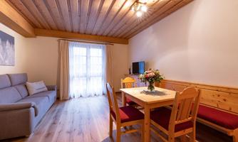 A cozy living room with a sofa, a table, and chairs. Large windows let in plenty of light.