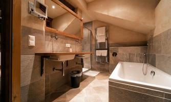 A modern bathroom with a bathtub and an elegant sink. The walls are covered with gray tiles and wooden paneling.