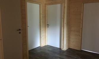 A bright room with wooden walls and several white doors. The floor is tiled with dark tiles.