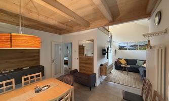 A modern living and dining room with wooden ceilings and pleasant lighting. The decor is cozy and stylish, featuring a dining area and a seating corner.