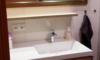 A modern bathroom with a wooden vanity and a mirror. The room has bright lighting and a minimalist design.
