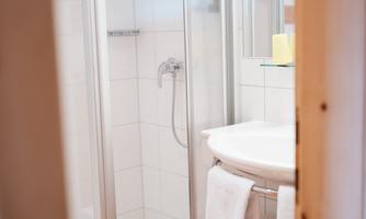 A modern bathroom with a shower cabin and a sink. Fresh towels and toiletries are visible.