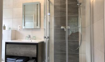 A modern bathroom with a glass shower and a sink. The walls are brightly tiled, and there are some towels and toiletries.