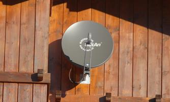 A satellite dish on a wooden-paneled wall. It is round and gray, with a white logo on it.