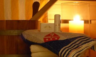 A relaxing wellness area with towels, care products, and a burning candle. In the background, wood and striped towels are visible.