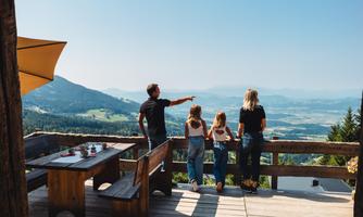 A family stands at an observation point and looks at the magnificent mountain landscape. The sky is clear and the landscape is green and picturesque.