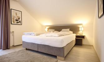 A cozy bedroom with a large bed and soft lighting. The walls are bright and decorated minimally.