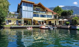 A beautiful house by the water with a modern design. In the foreground, there are boats and people relaxing.