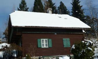 A cozy wooden house in the snow, surrounded by trees. The snow covers the roof and the ground of the house.