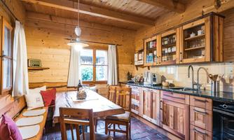 A cozy wooden kitchen with a large dining table and comfortable benches. The walls and furniture exude rustic charm.