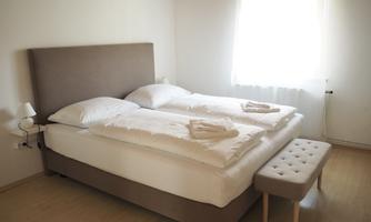 A cozy bedroom with a large double bed and bright windows. The room is simply and modernly furnished.