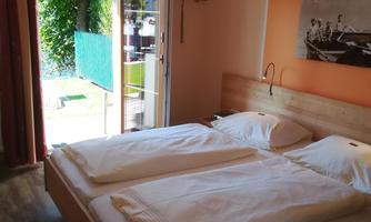 A cozy bedroom with a large double bed and colorful curtains. The room has access to a balcony with a view of the garden.
