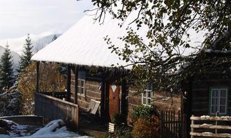 A traditional wooden house with a snow-covered roof. Surrounded by trees and a wintry landscape.