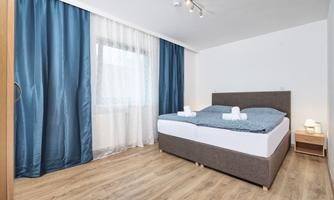 A modern bedroom with a large bed and fresh bedding. The curtains are blue and the walls are light, creating an inviting atmosphere.