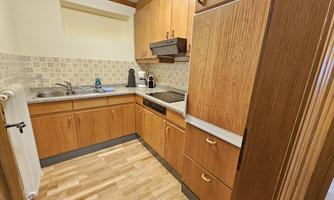 A modern kitchen with wooden cabinets and bright tiles. It features a sink, a stove, and a refrigerator.