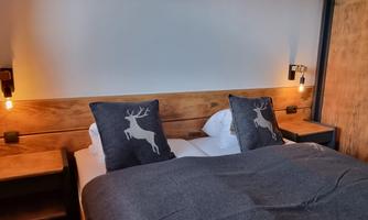 A cozy bedroom with a double bed and decorative cushions. The walls are in neutral colors, and the lighting creates a warm atmosphere.