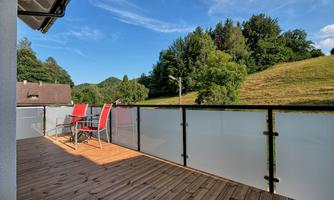A beautiful balcony with two red chairs and a wooden floor. In the background, green hills and trees can be seen.